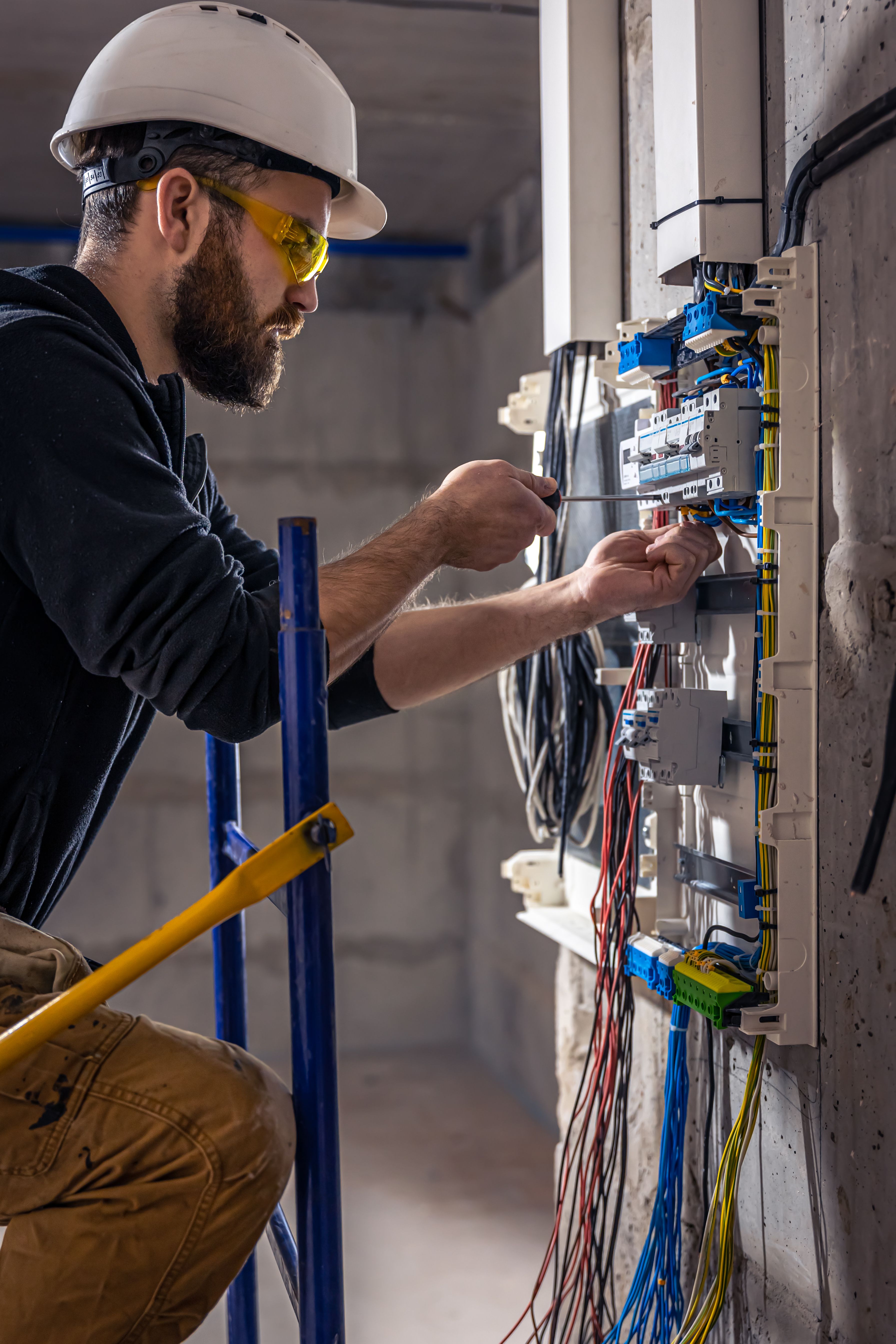 Professional electrician working on a switchboard with electrical connecting cable